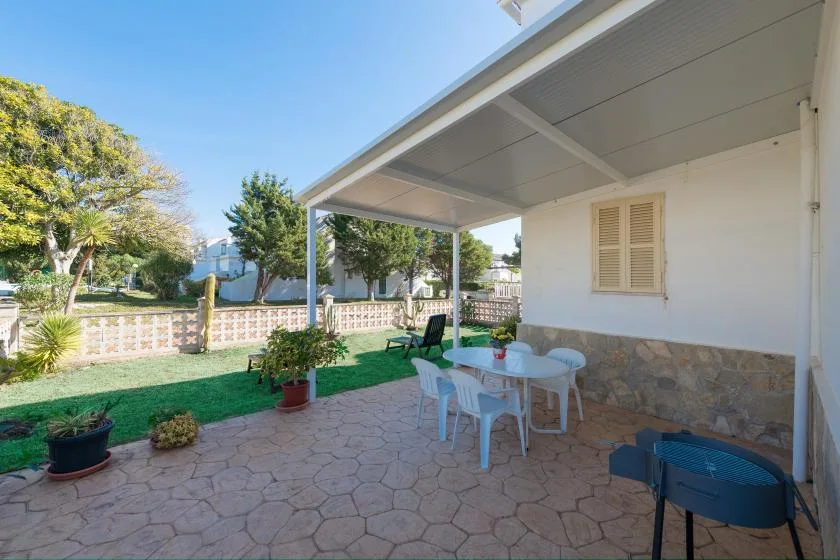 A covered patio with a table and seating overlooks a garden.
