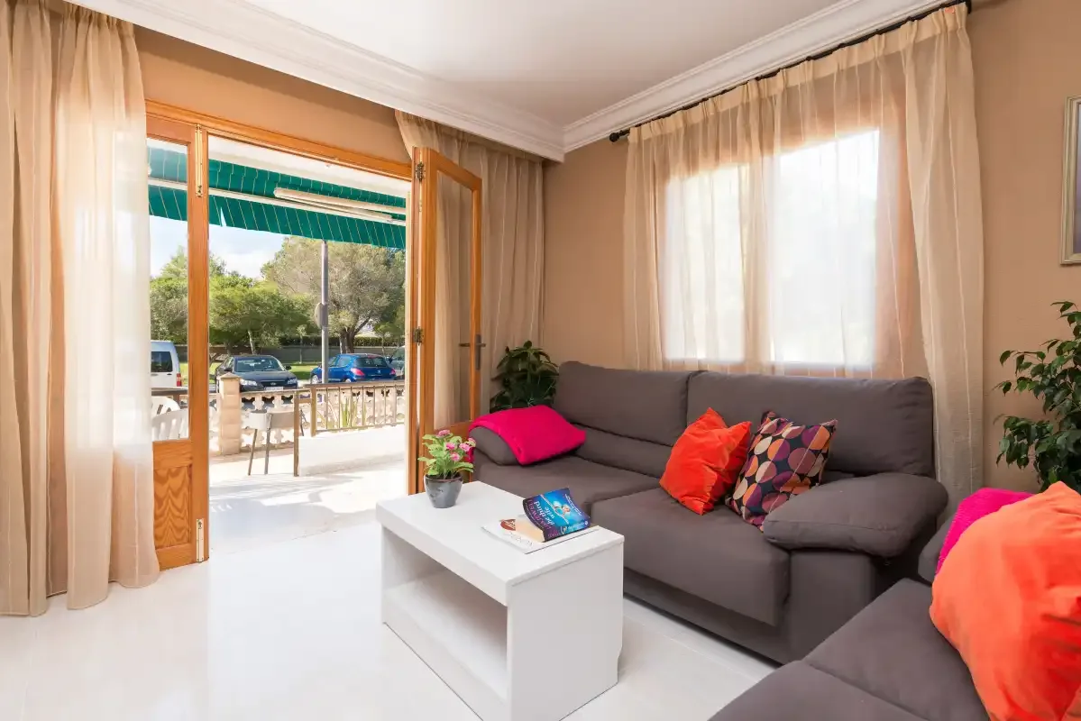 A living room with seating, a coffee table, and an open door to the balcony.