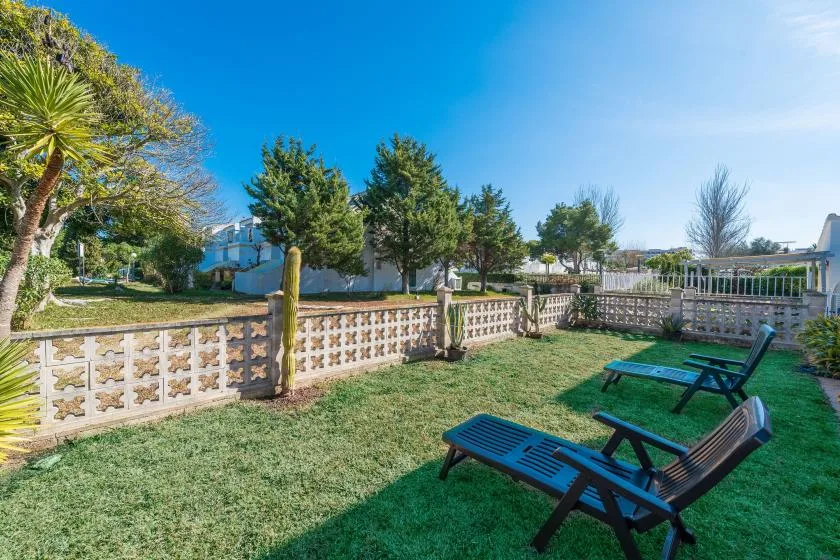 A grassy outdoor seating area sits beside a decorative fence and trees.