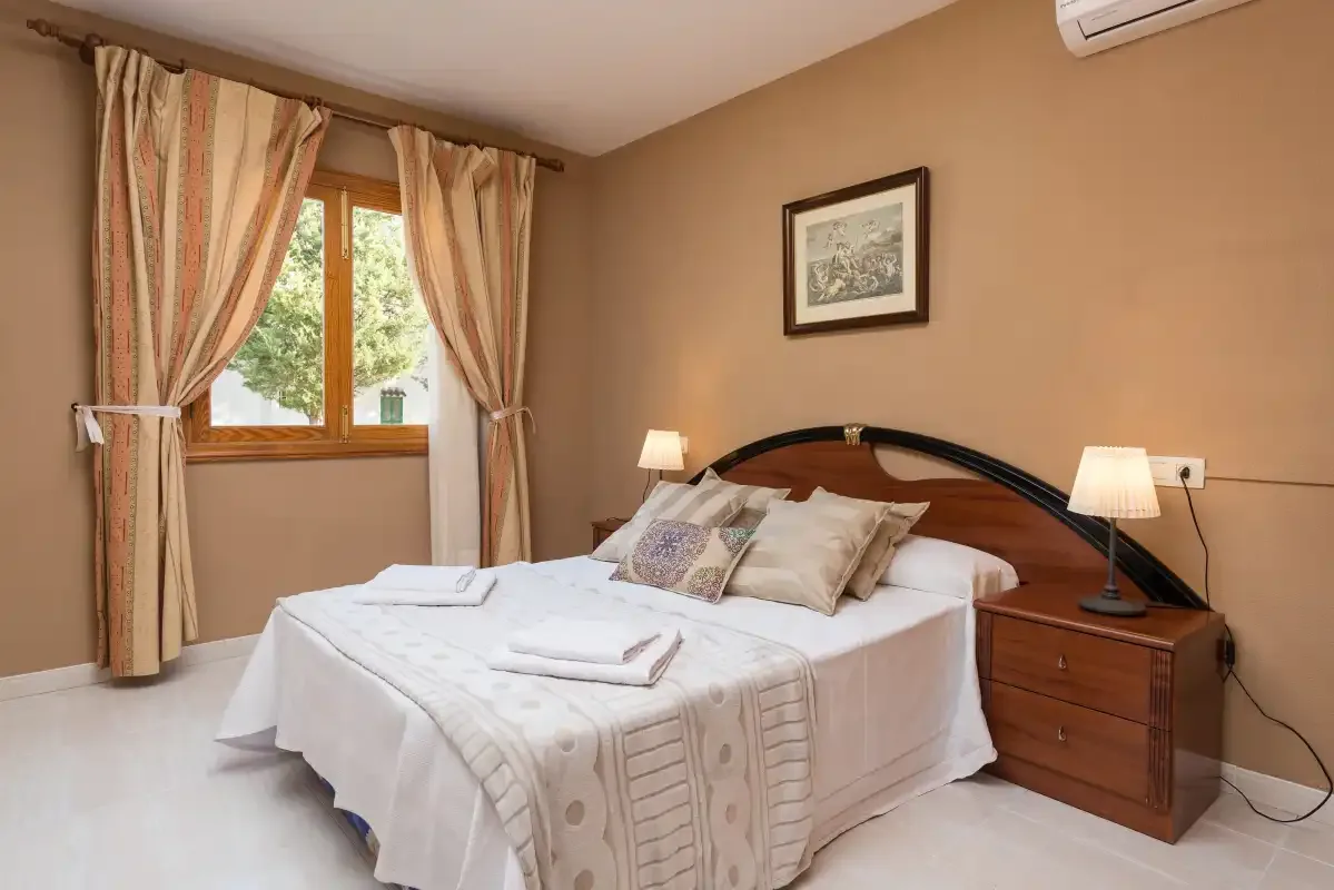 A bedroom with a neatly made bed, bedside tables, and a curtained window.