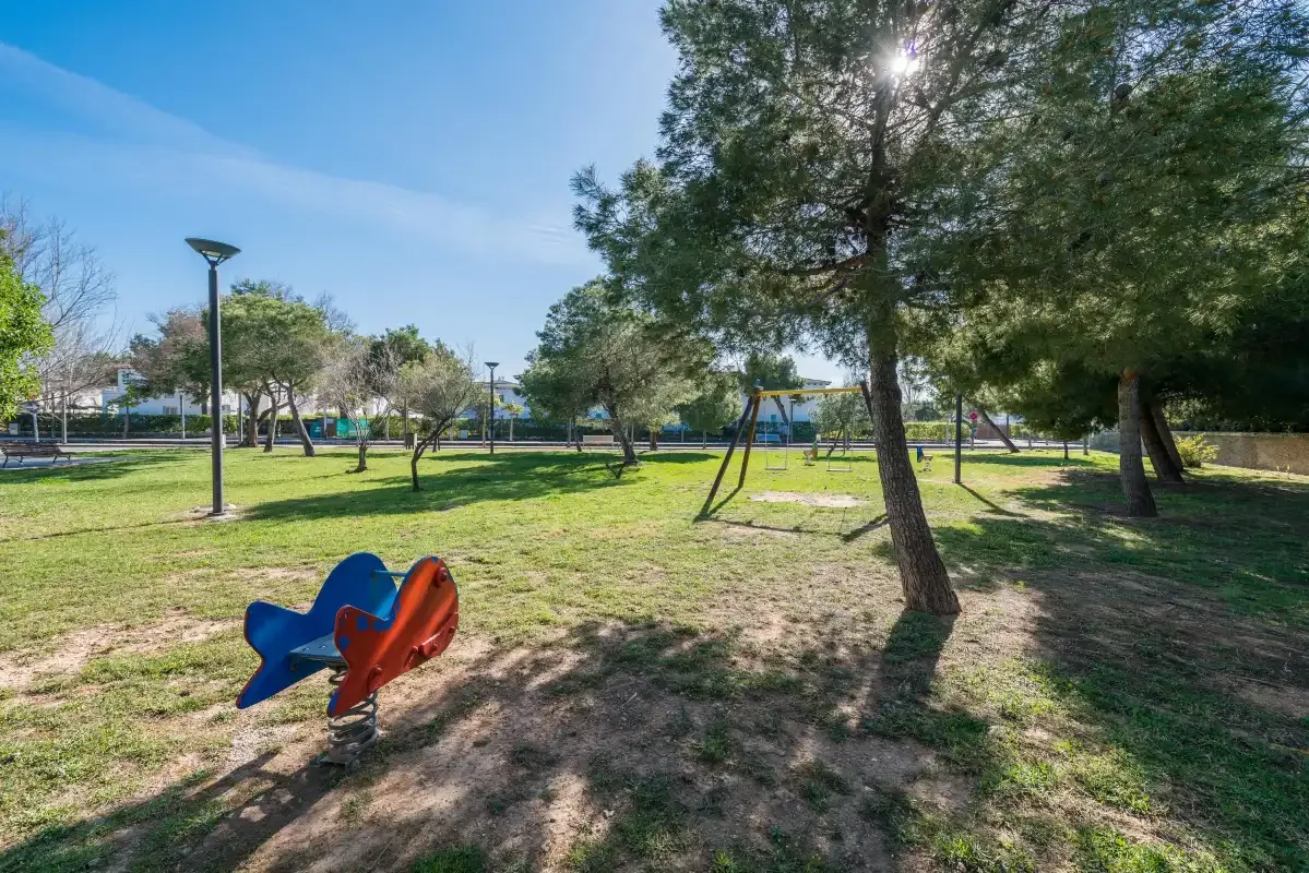 A grassy outdoor play area with playground equipment and large trees.