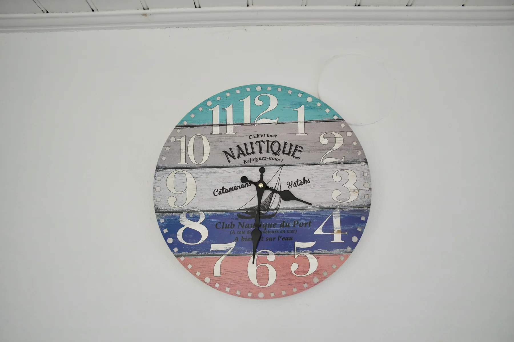 A nautical wall clock hangs on a plain white wall.