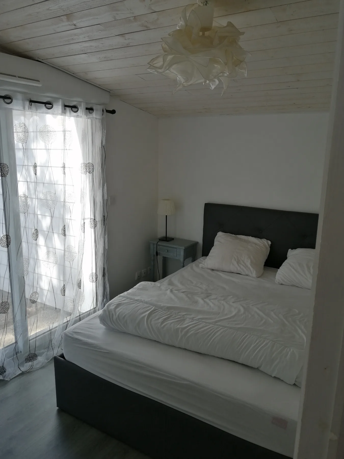 A bedroom with a bed and sheer curtains beside a glass door.