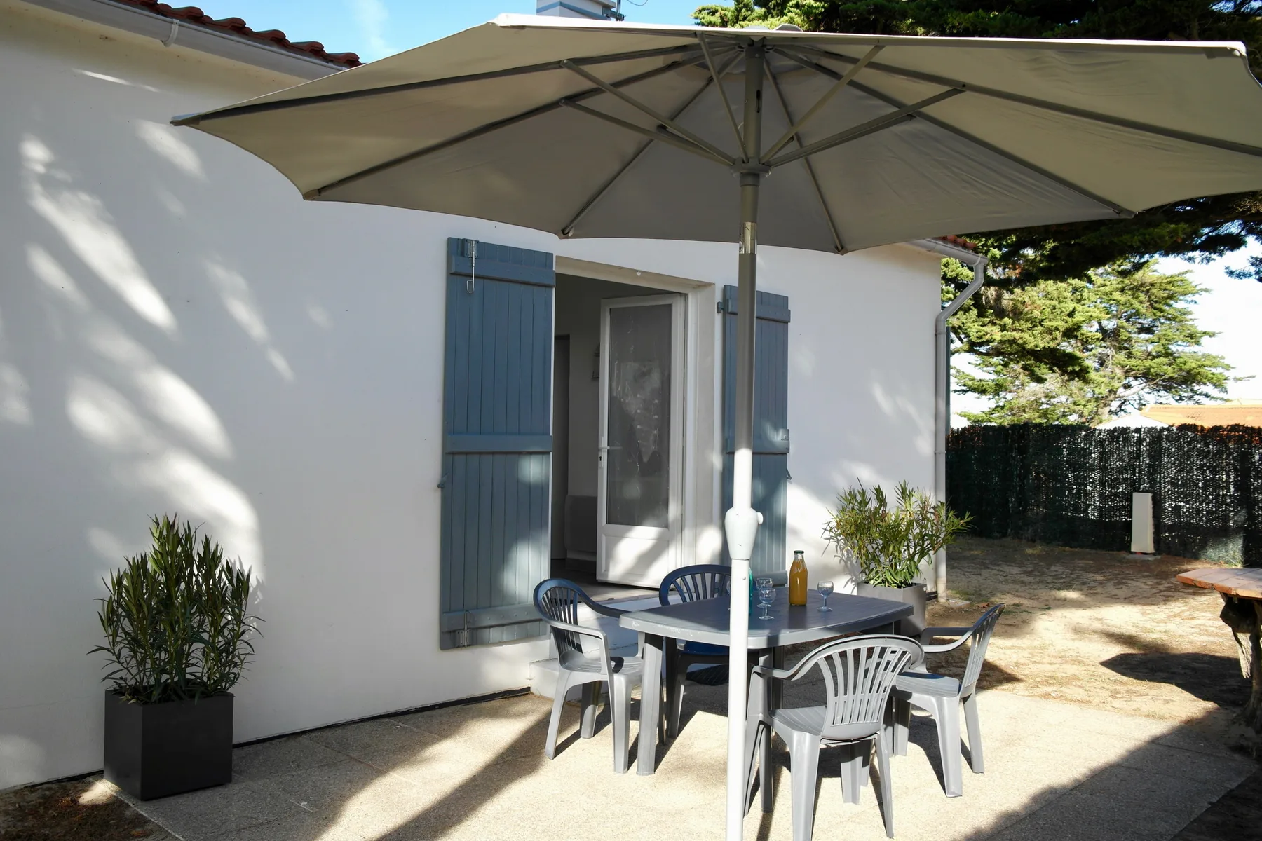 A sunny outdoor patio with a table and seating beneath a large umbrella.