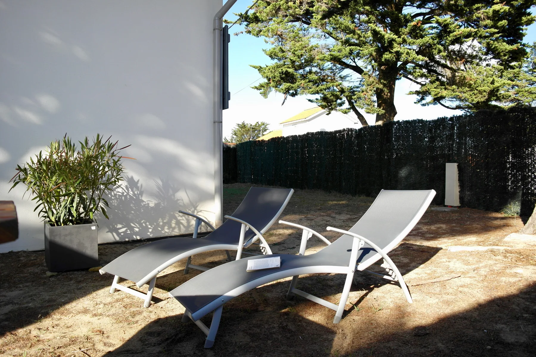 Outdoor seating beside a white wall, with a tree and garden fence in the background.