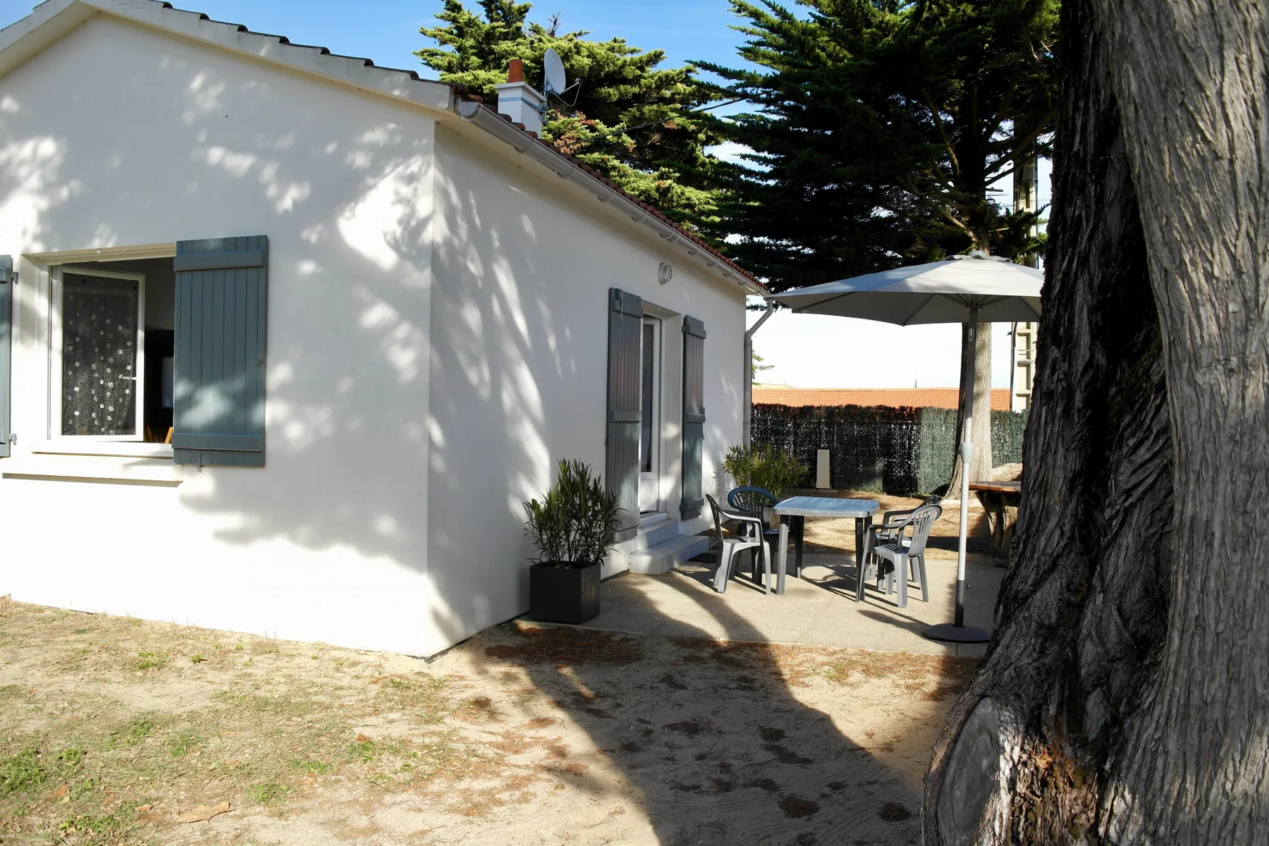A white house opens onto a shaded patio with outdoor seating.