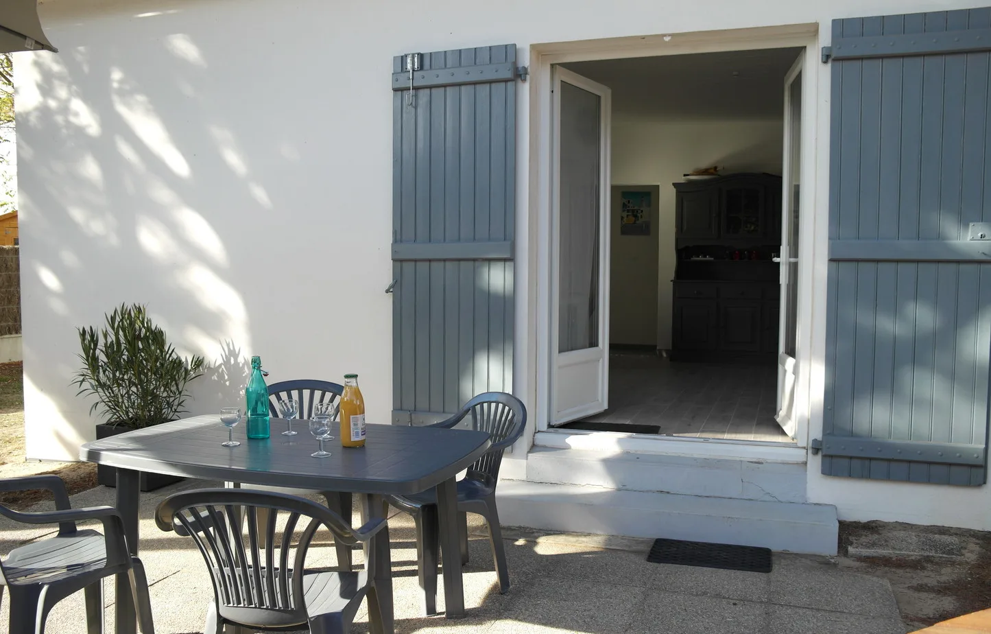 An outdoor dining area sits beside an open doorway with blue shutters.