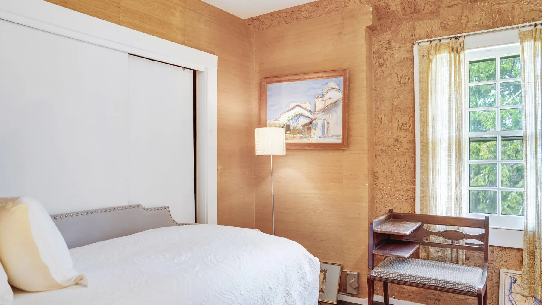 Un dormitorio con una cama, una ventana y una pequeña estantería.