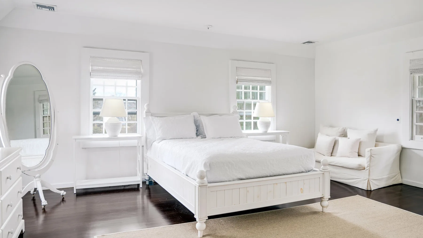 Un dormitorio luminoso con una cama blanca y una pequeña zona de estar.
