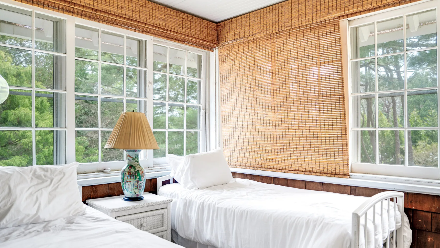 Un dormitorio luminoso con dos camas y grandes ventanas con vistas a la vegetación.