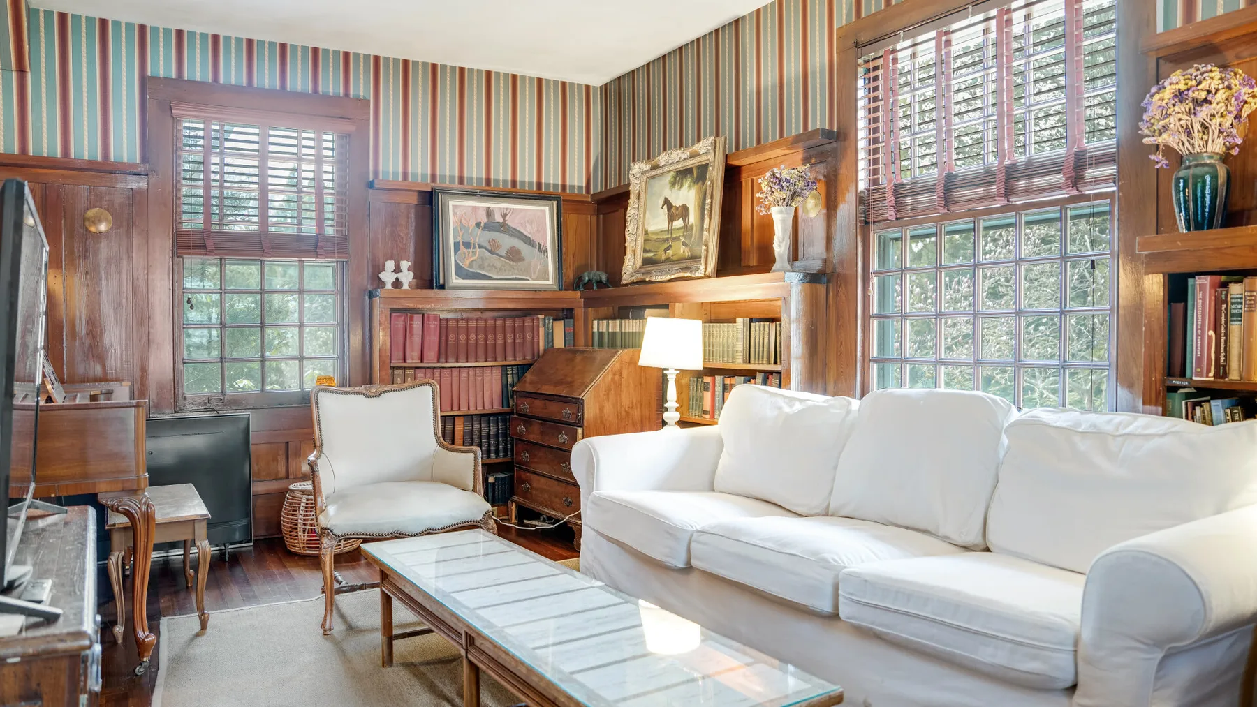 Una sala de estar con asientos blancos, estanterías y ventanas grandes.
