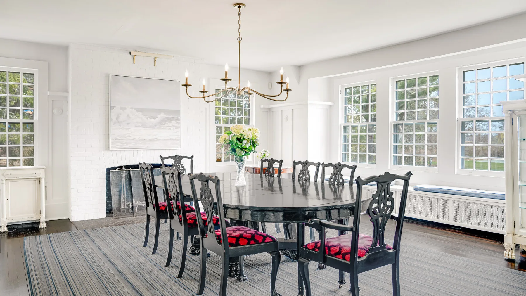 Un comedor luminoso tiene una mesa larga y sillas oscuras junto a grandes ventanas.