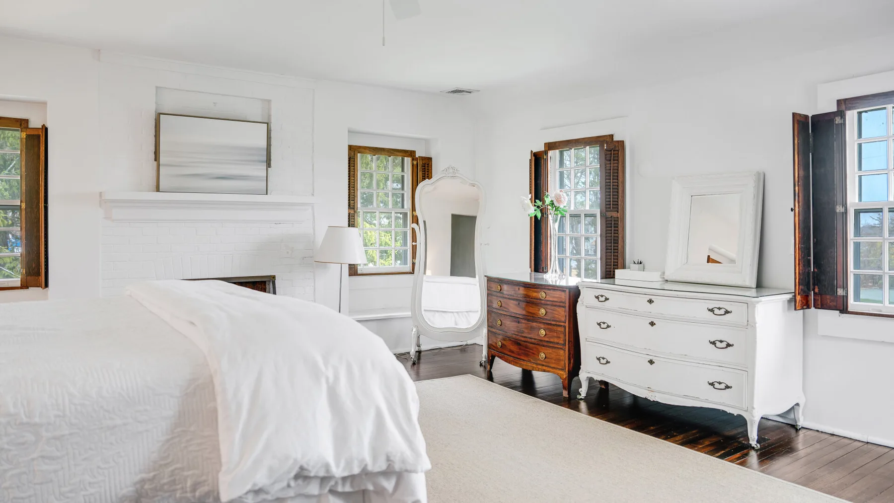 Un dormitorio luminoso con una cama, una cómoda y varias ventanas altas.