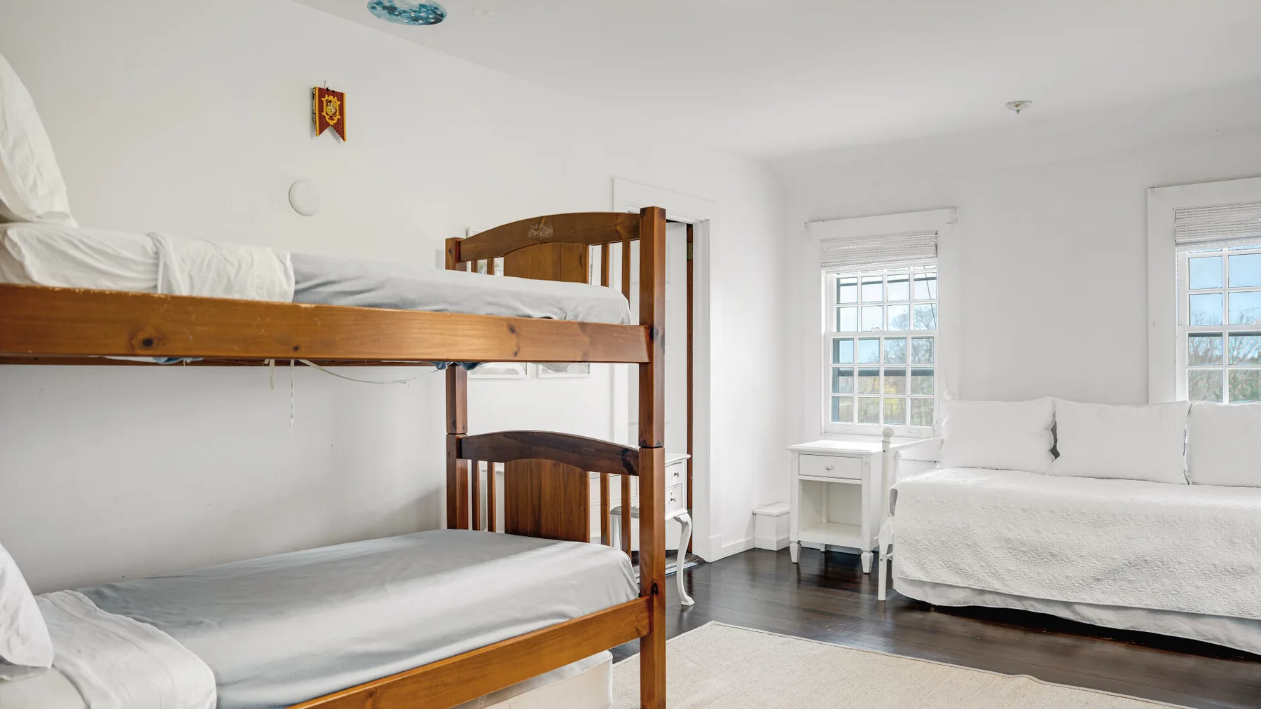 Un dormitorio luminoso con una litera de madera y otra cama junto a las ventanas.