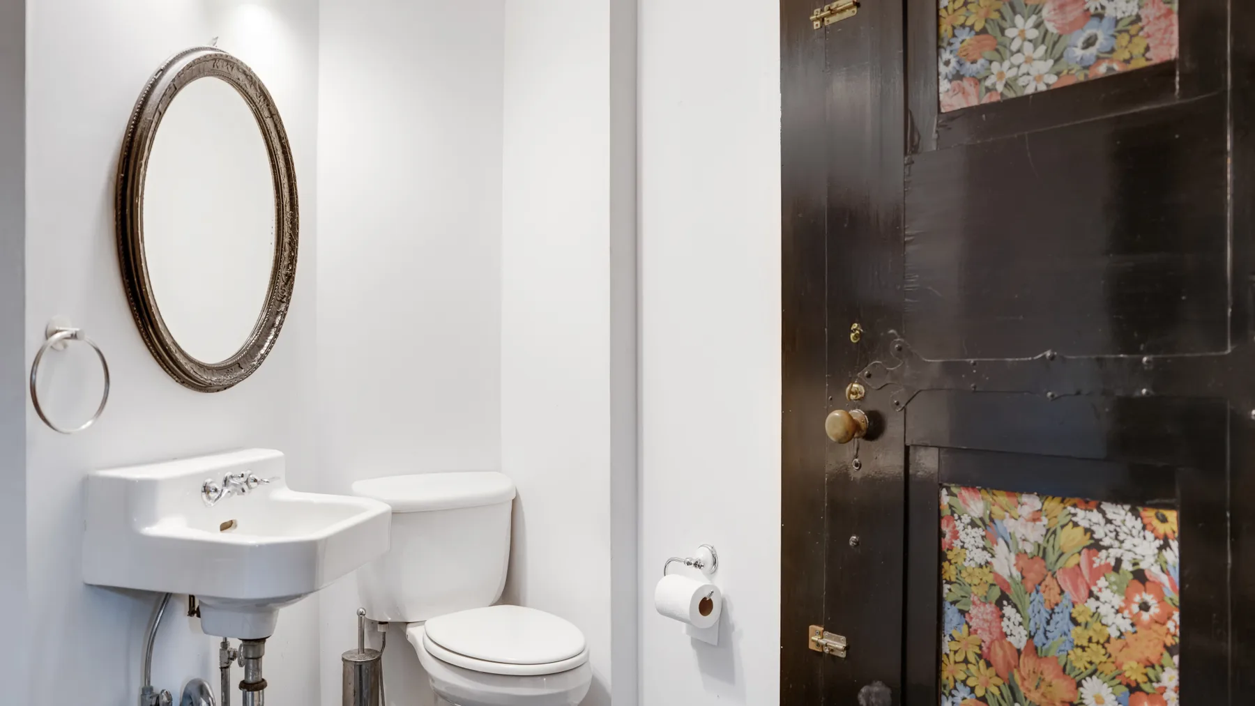 Un baño con lavabo de pared, inodoro y una puerta oscura.