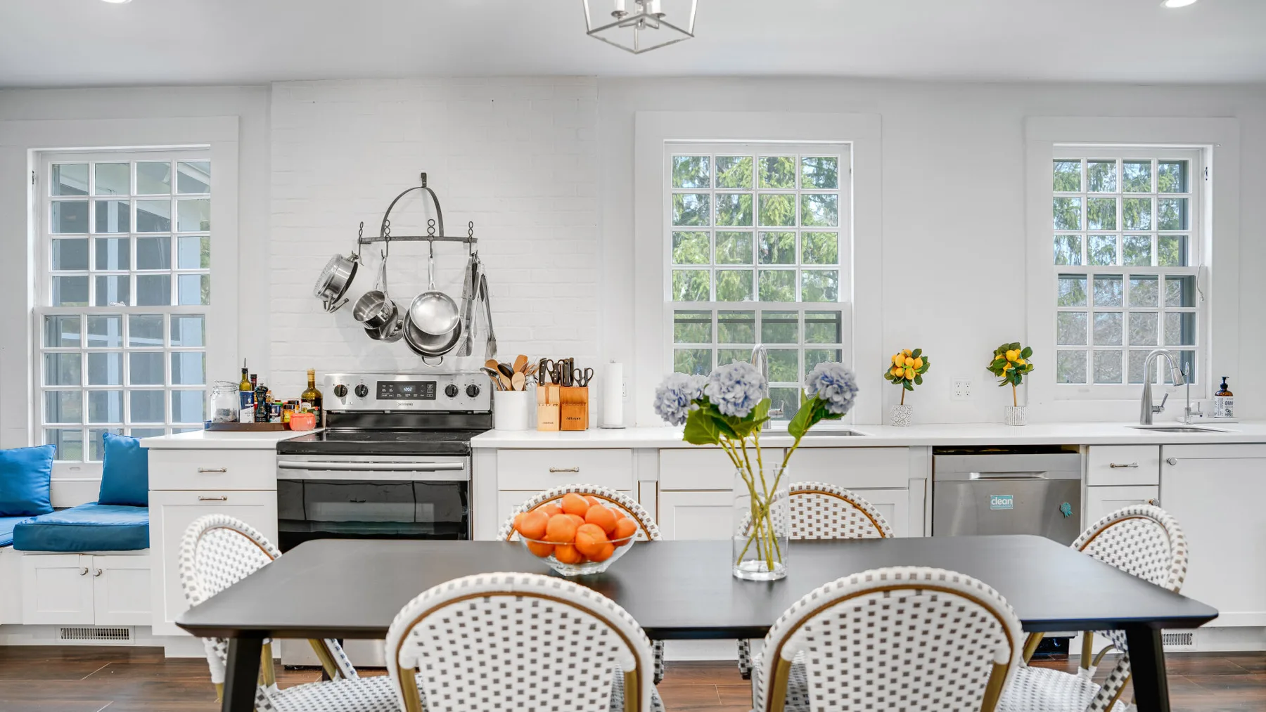 Una cocina luminosa con mesa de comedor, gabinetes blancos y ventanas.