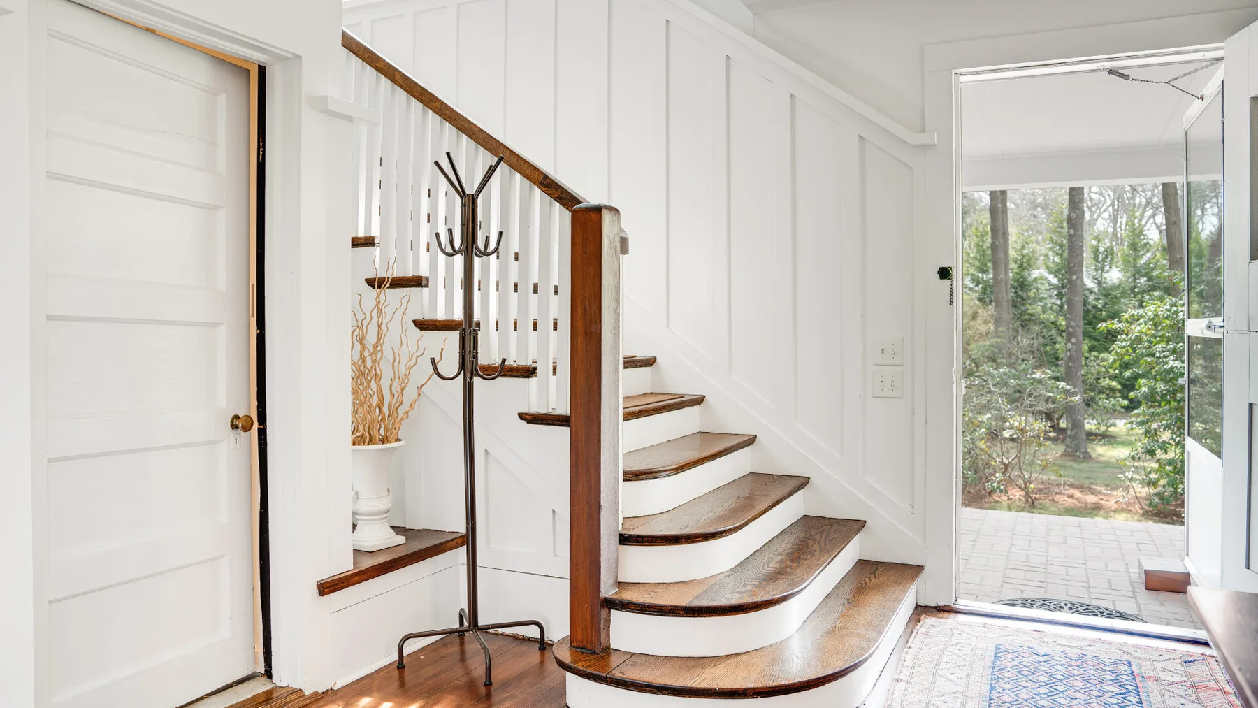 Un pasillo interior luminoso con una escalera curva y una puerta de vidrio abierta hacia la vegetación.