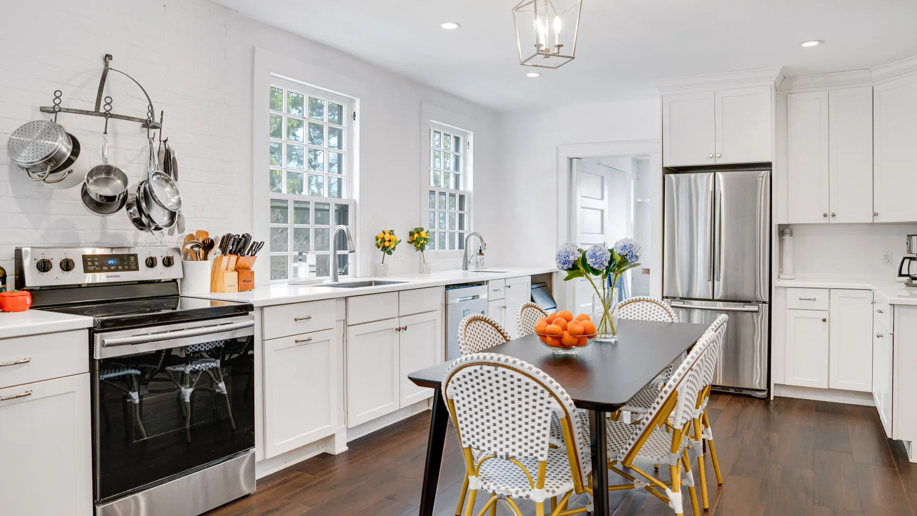 Una cocina luminosa con zona de comedor, armarios blancos y una mesa oscura.