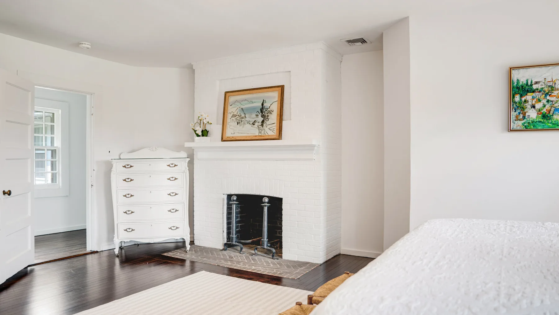 Un dormitorio luminoso con chimenea, cómoda y cuadros enmarcados.