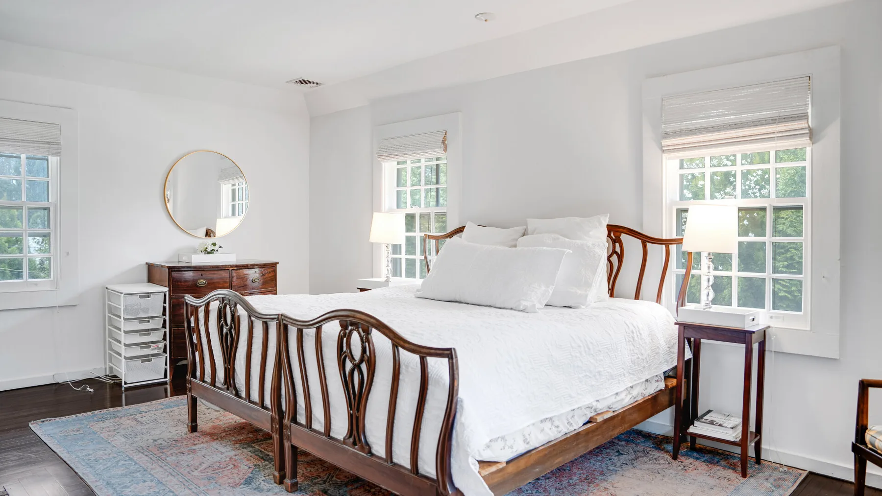 Un dormitorio luminoso con una cama grande, mesitas de noche y ventanas altas.