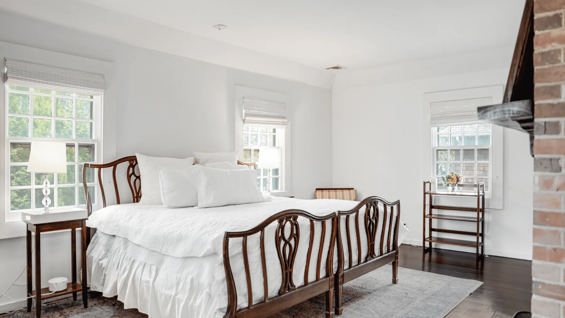 Un dormitorio luminoso con una cama blanca, estructura de madera oscura y ventanas.