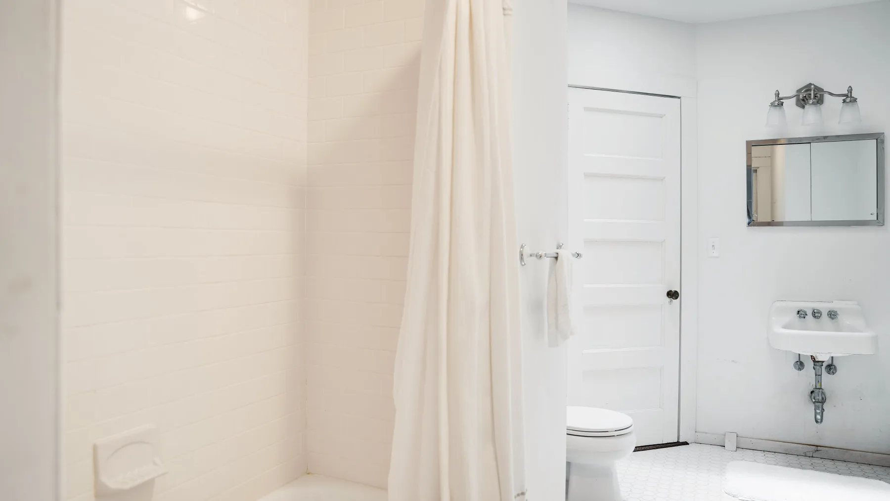 Un baño luminoso con cortina de ducha, inodoro y lavabo de pared.