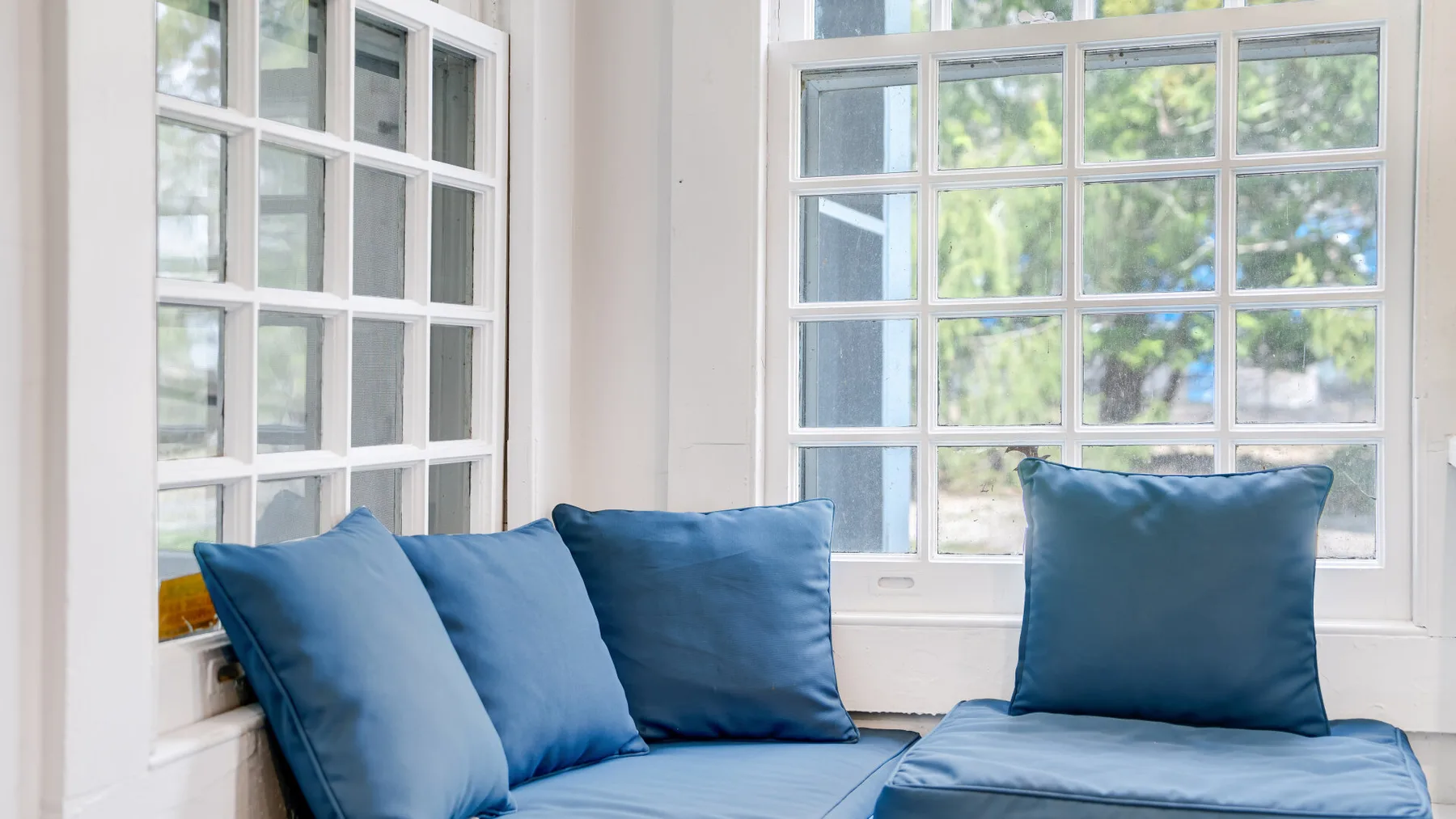 Una zona de estar luminosa con cojines azules junto a grandes ventanas.