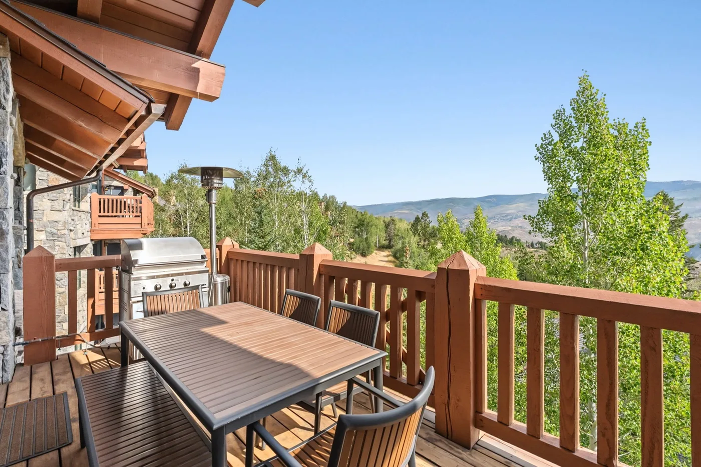 A wooden deck with a dining table overlooks trees and distant hills.