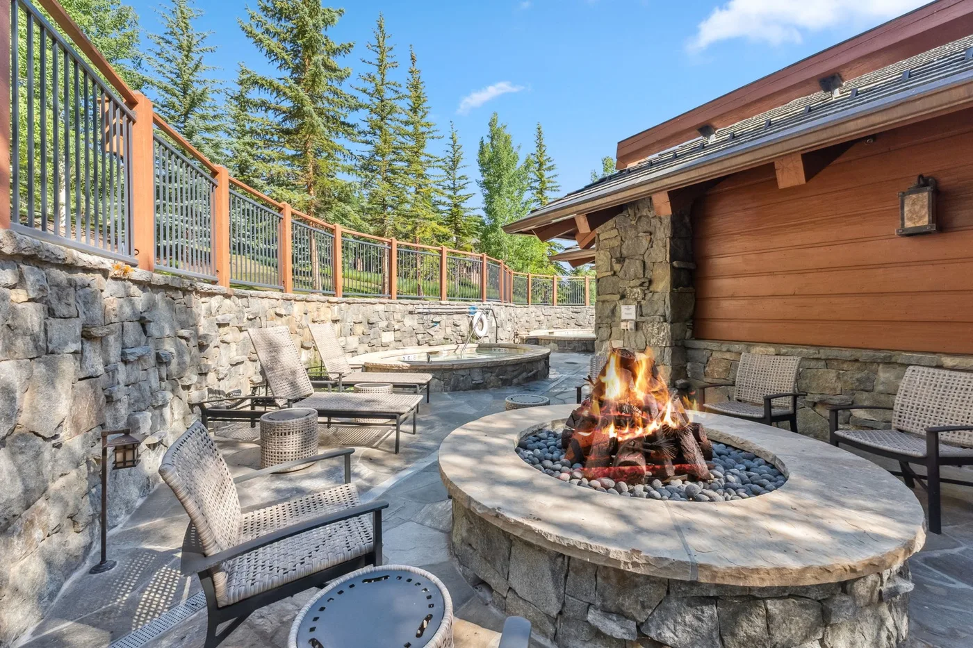An outdoor patio with seating surrounds a circular fire pit beside a stone wall.