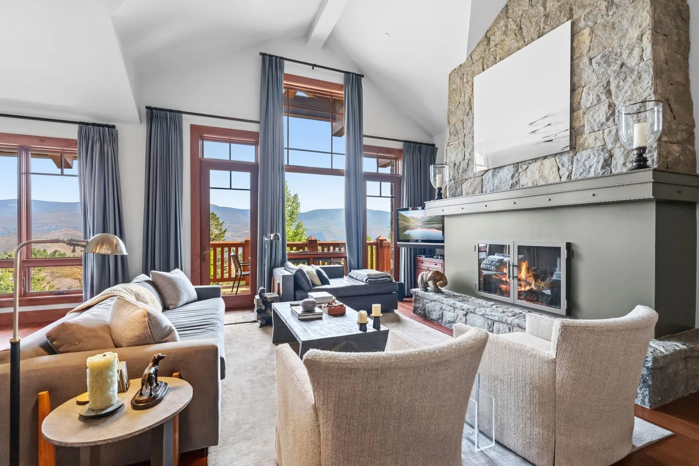A living room with seating, tall windows, and a stone fireplace.