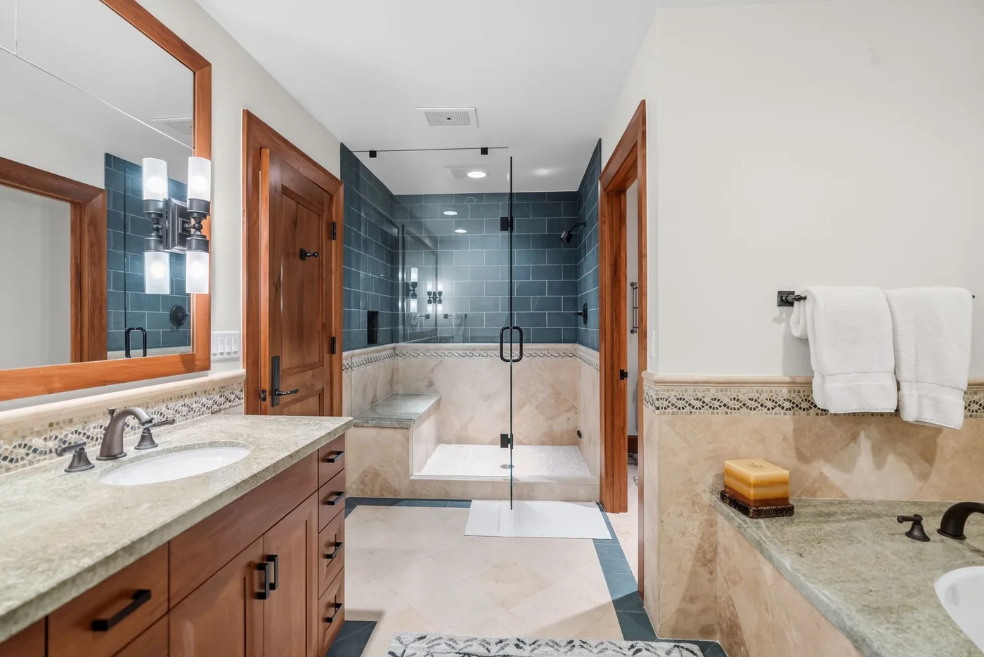 A bathroom with a glass shower, a stone vanity, and towels hanging on the wall.