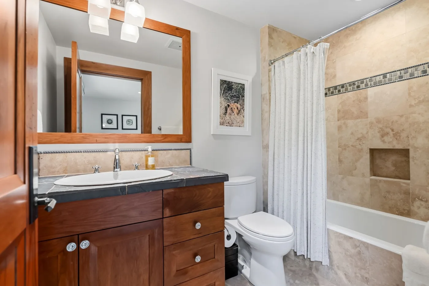 A bathroom with a wooden vanity, toilet, and curtained bathtub.