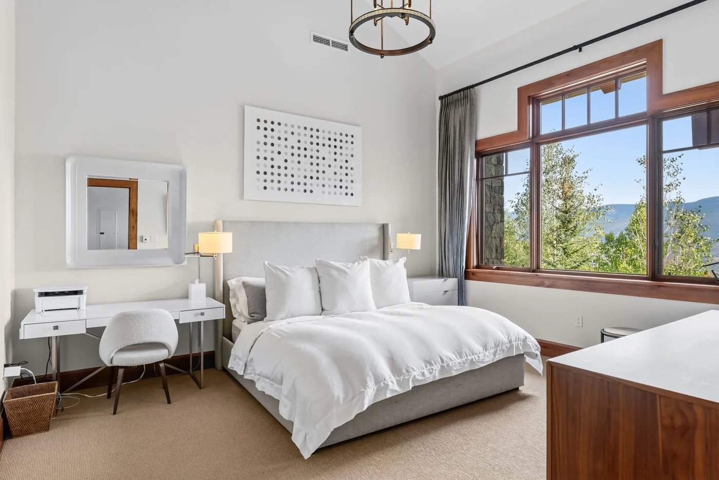 A bedroom with a large bed, bedside tables, and a desk beside a wide window.