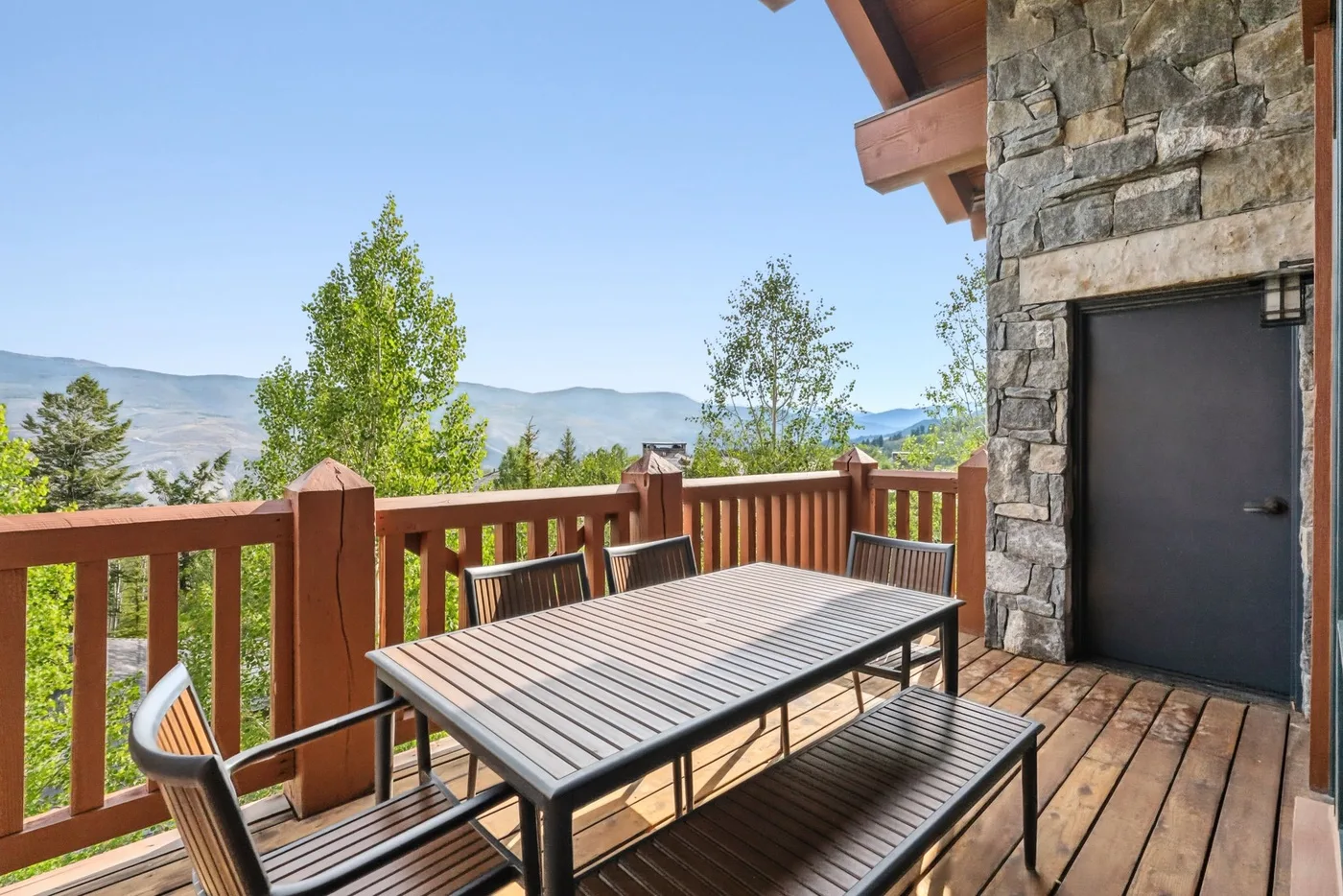 A wooden deck with outdoor seating overlooks trees and distant hills.