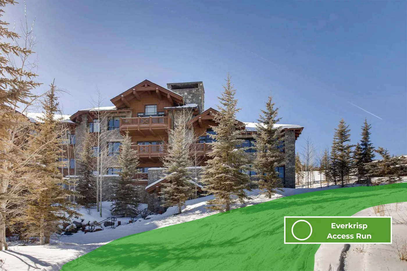 A multi-story lodge stands among snow-covered evergreen trees beside a ski run.