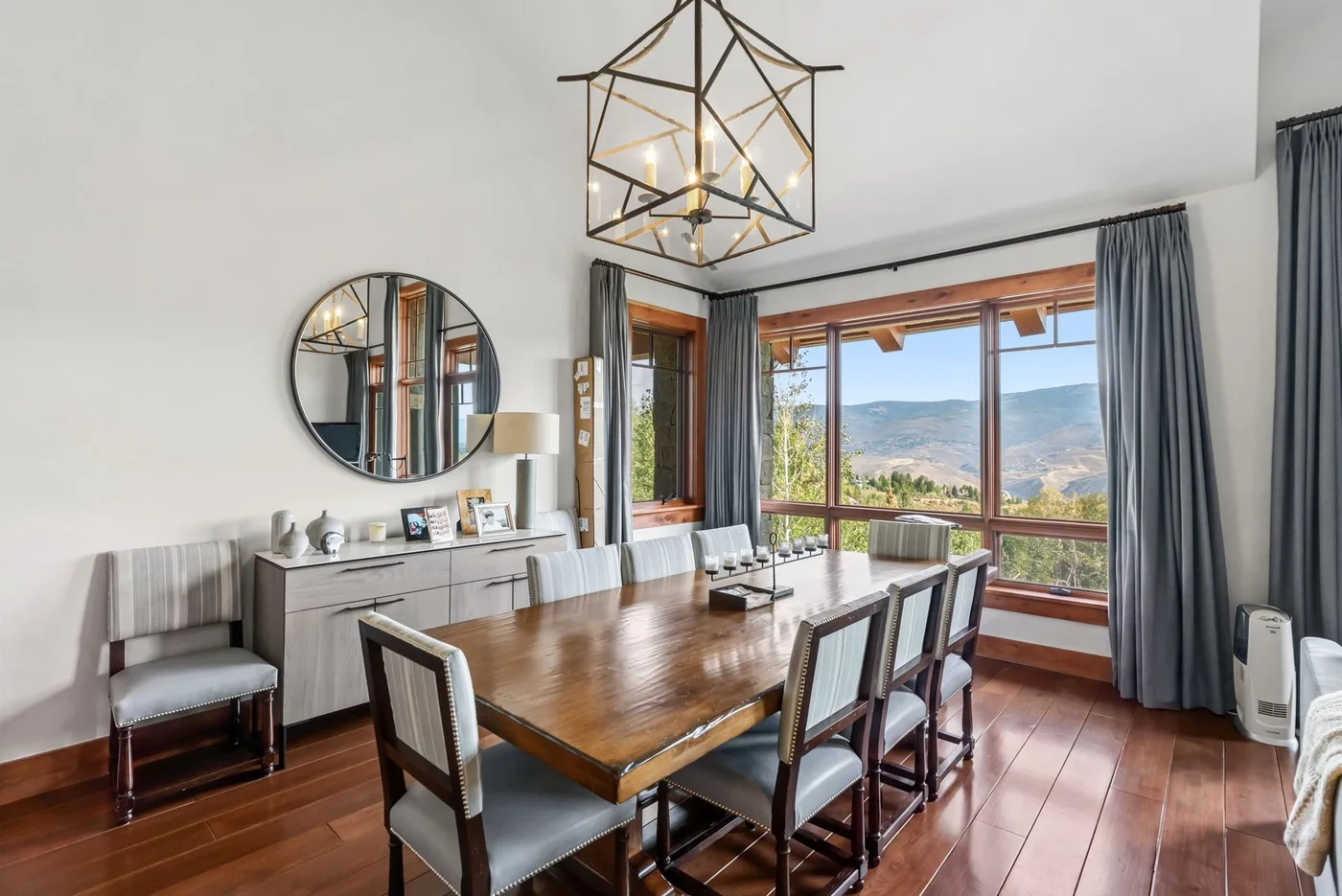 A dining room with a long wooden table beside large windows overlooking a valley.