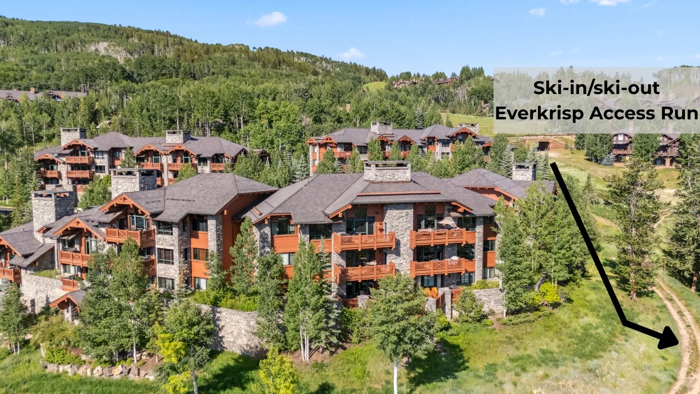 A cluster of lodge-style buildings sits on a green, wooded hillside.