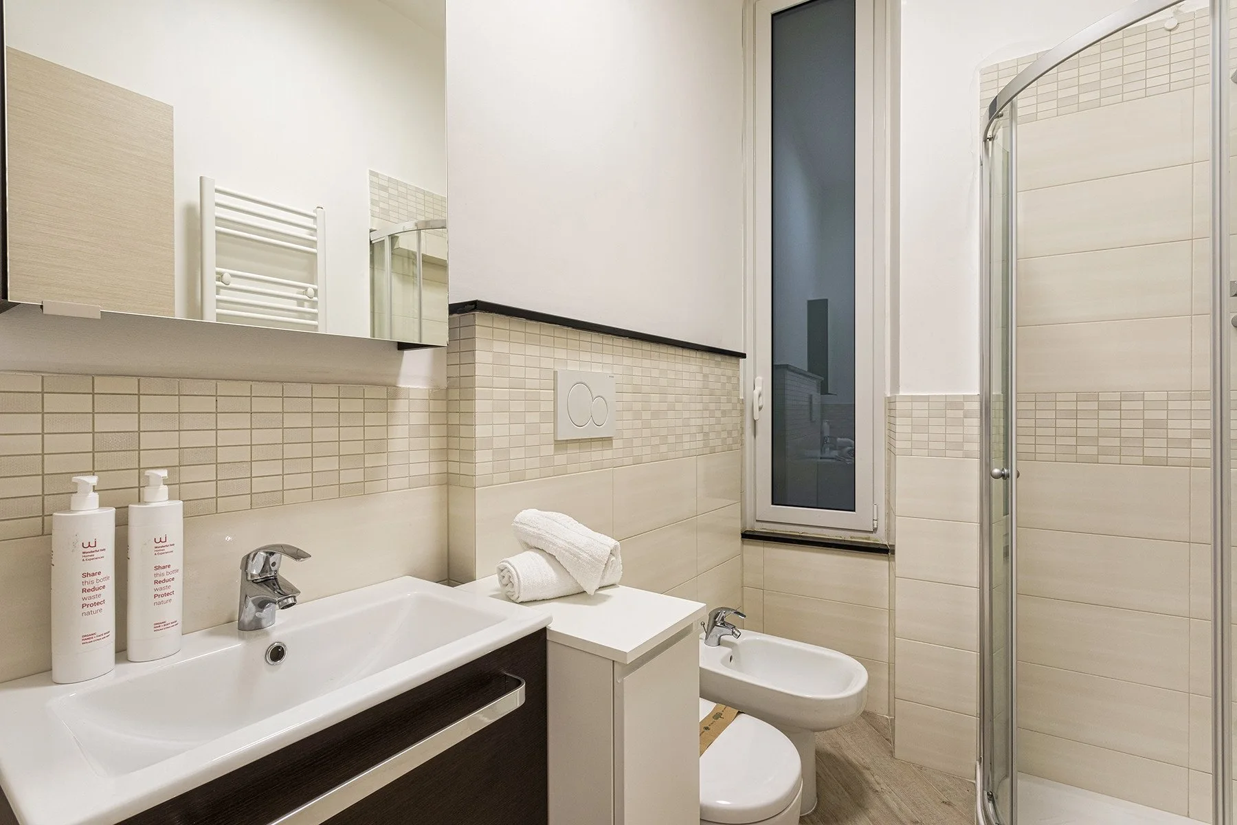 Un baño con azulejos, lavabo, inodoro y ducha con mampara de vidrio.
