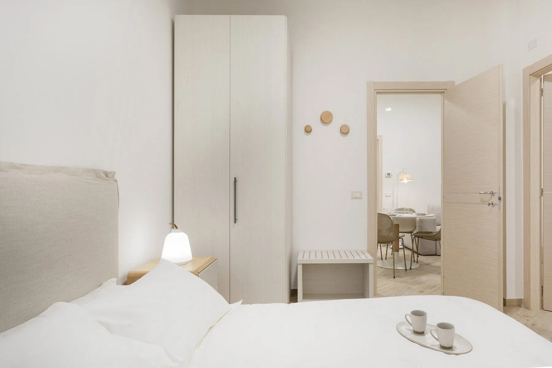 A bright bedroom with a bed, a tall wardrobe, and an open doorway.