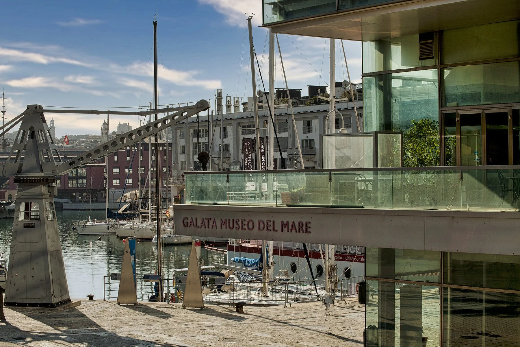 Un museo marítimo moderno con fachada de vidrio da a un puerto lleno de barcos y mástiles.