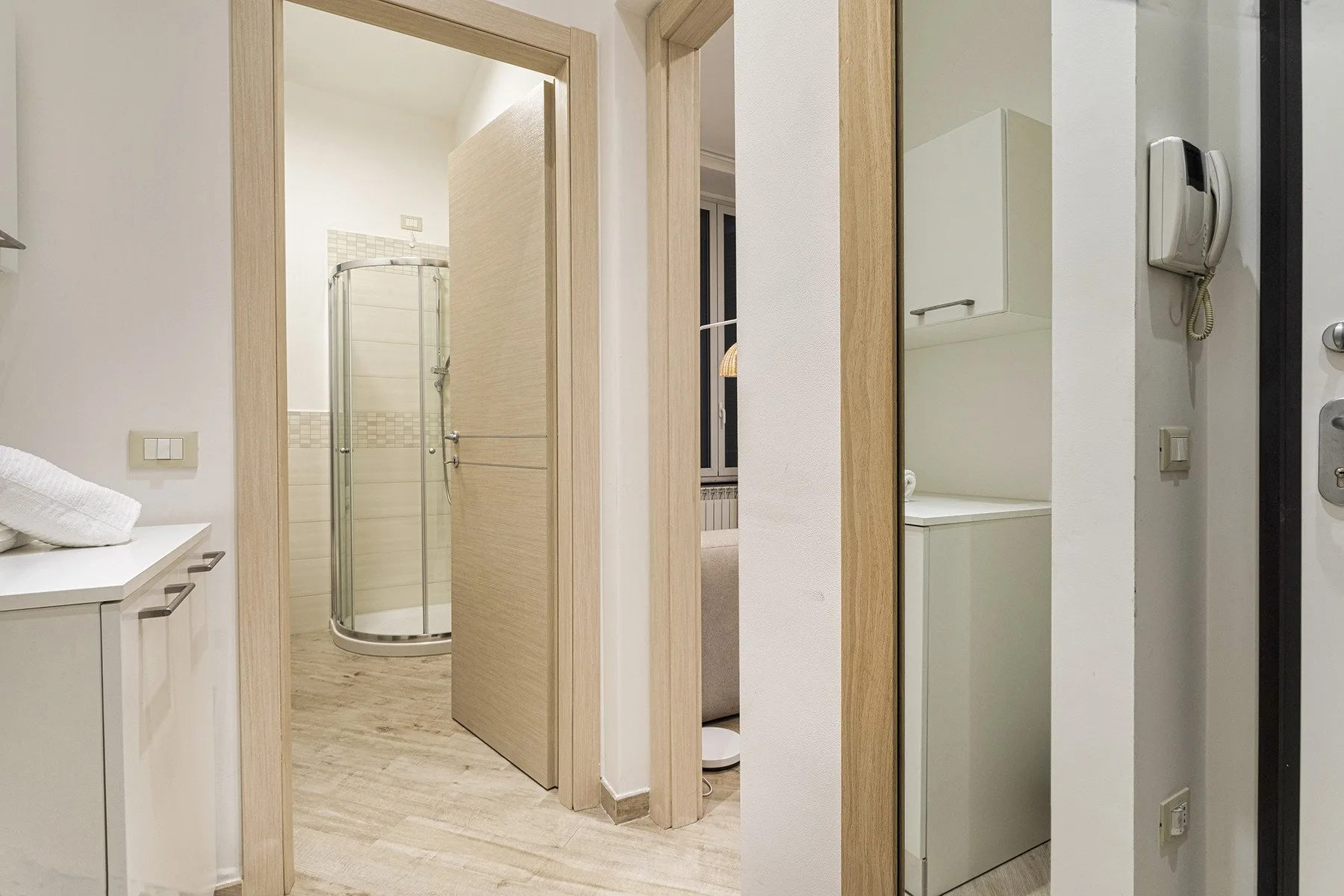 Un pasillo conecta un baño con ducha y una habitación con una cama.