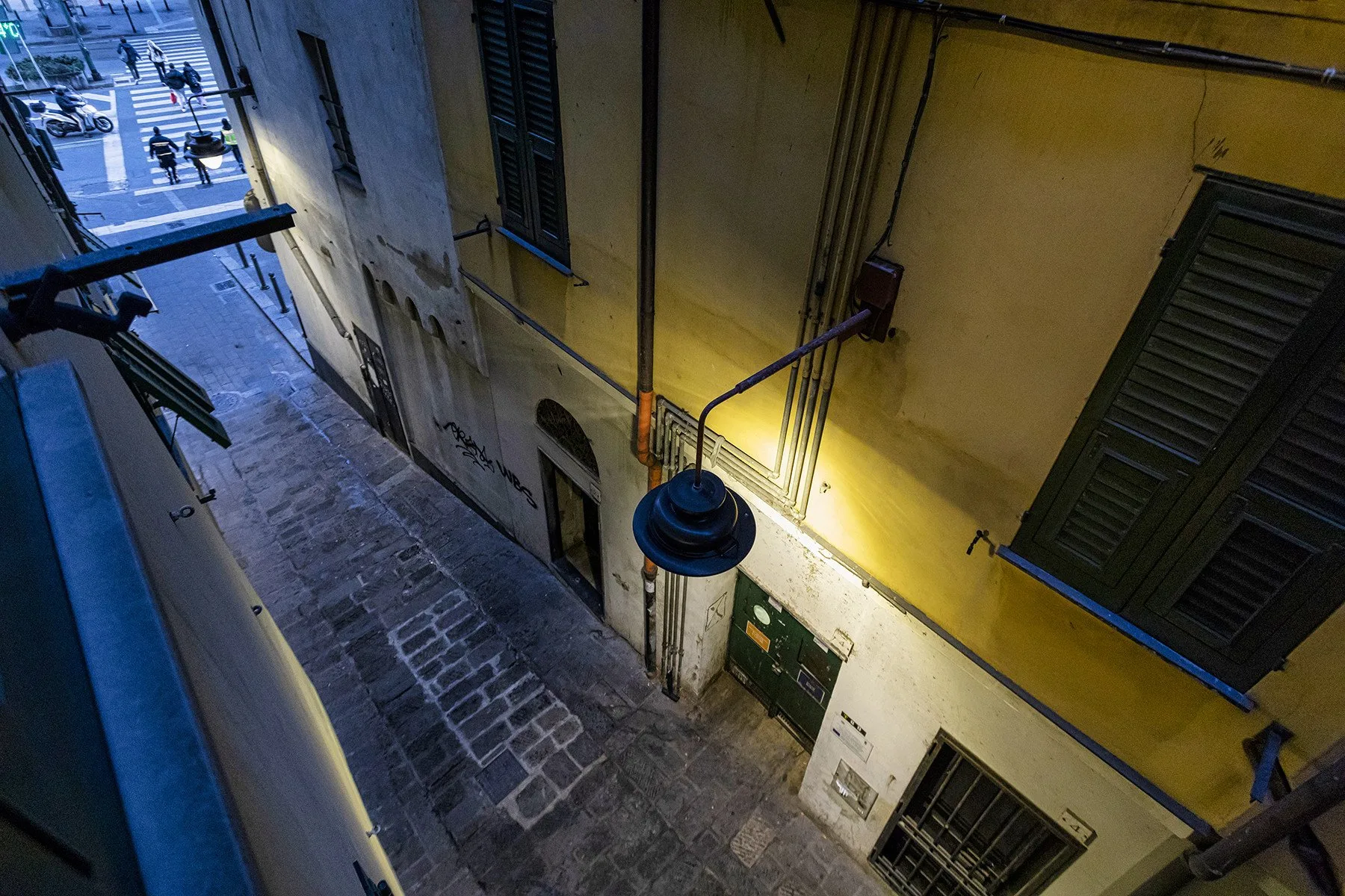 Una calle estrecha adoquinada discurre entre edificios altos, con una farola colgante.