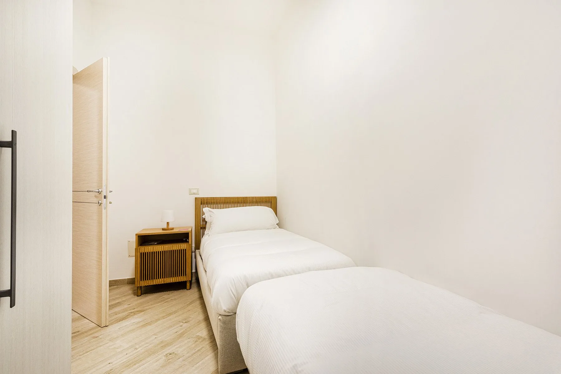 Un dormitorio luminoso con una cama blanca y una pequeña mesita de madera.
