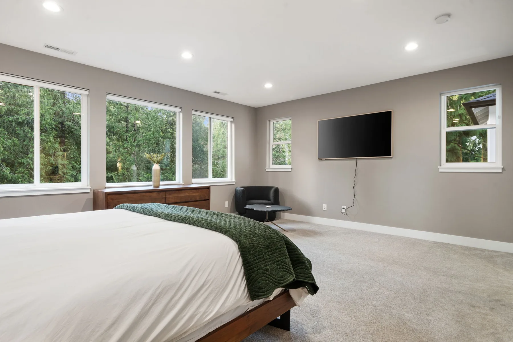 Un dormitorio con una cama, una manta verde y un televisor en la pared.