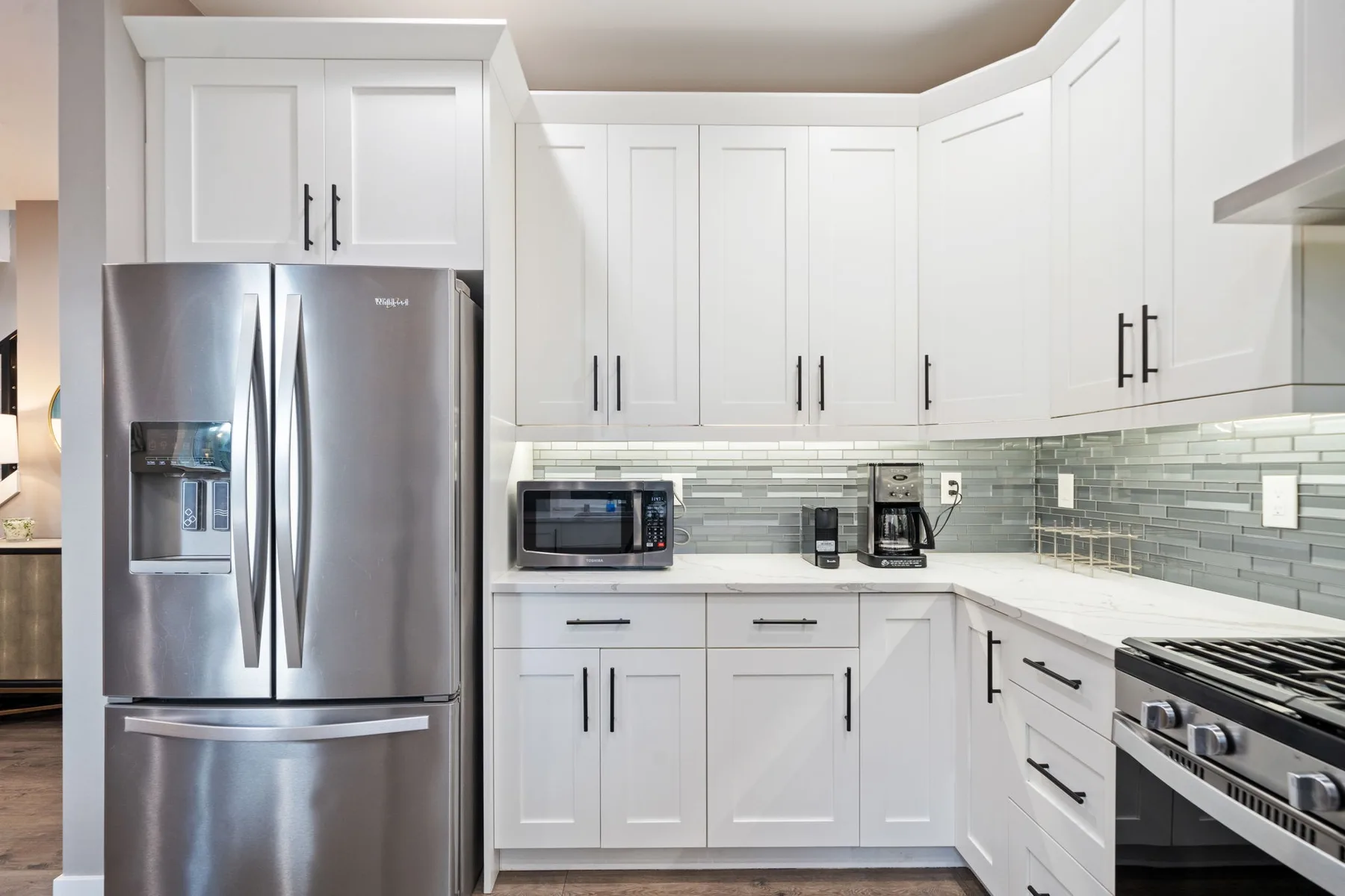 Una cocina luminosa con gabinetes blancos, electrodomésticos de acero inoxidable y un salpicadero de azulejos.