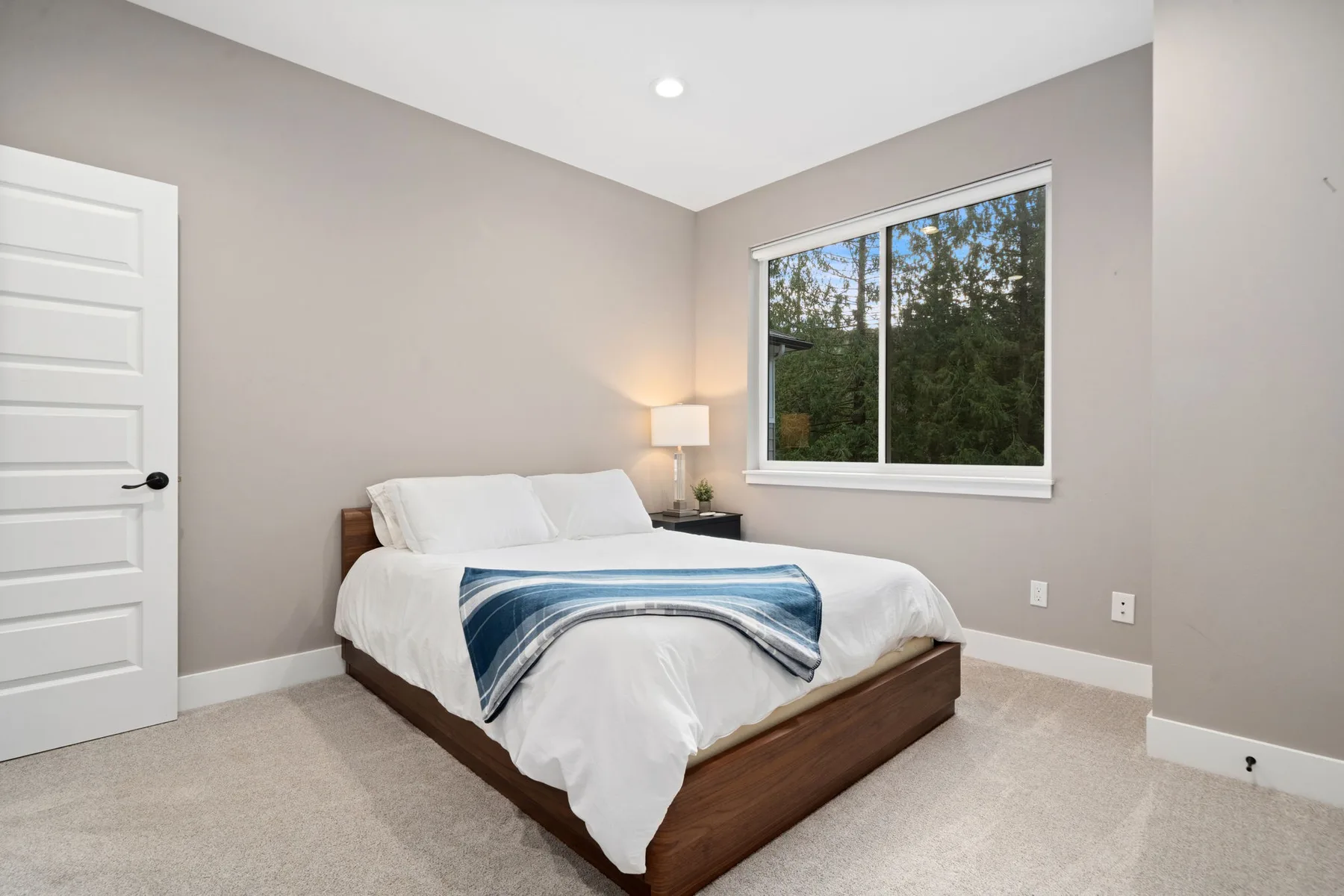Un dormitorio con una cama, ropa de cama blanca y una ventana con vista a los árboles.