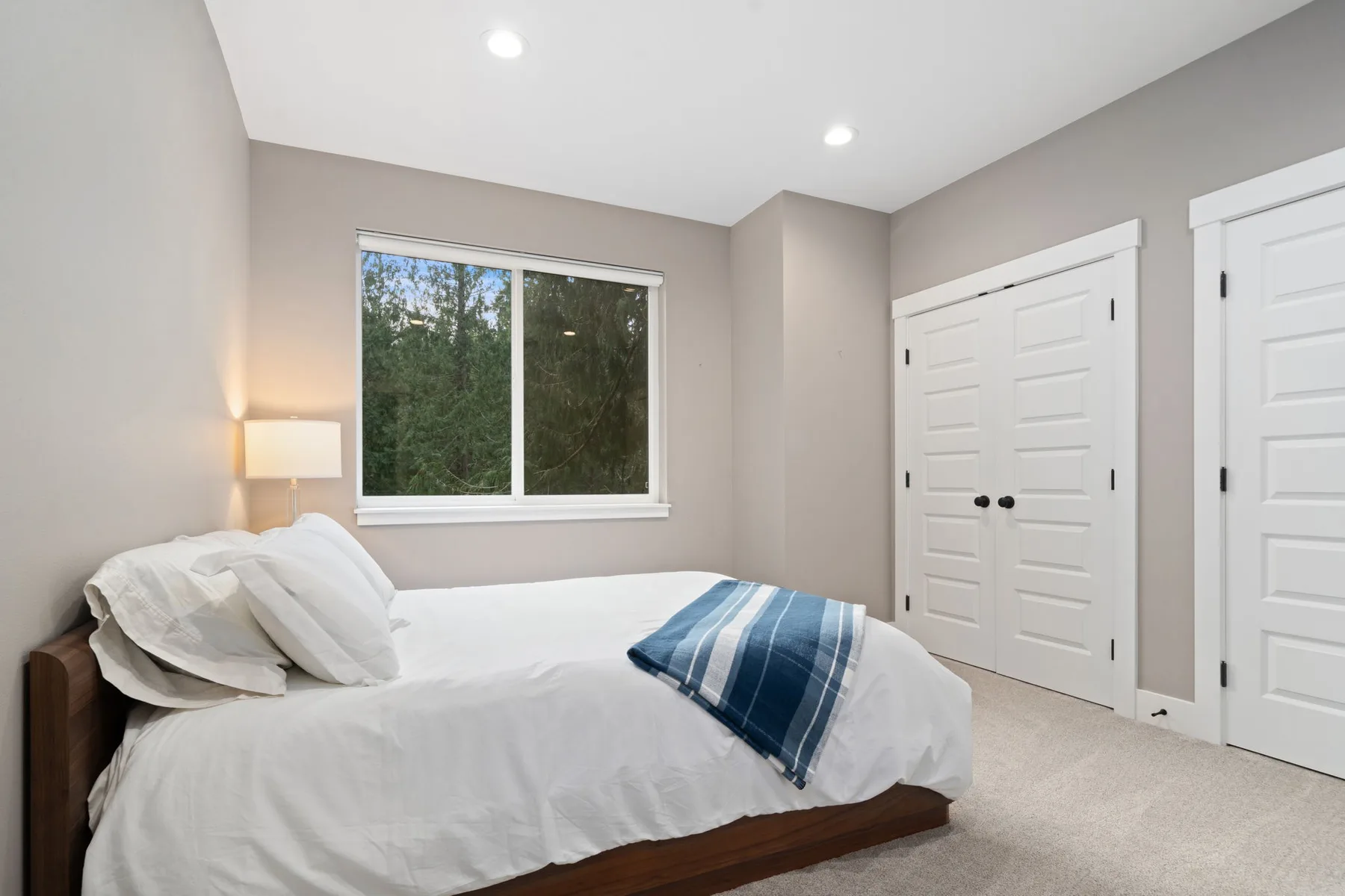 Un dormitorio con una cama, una ventana y puertas blancas de armario.