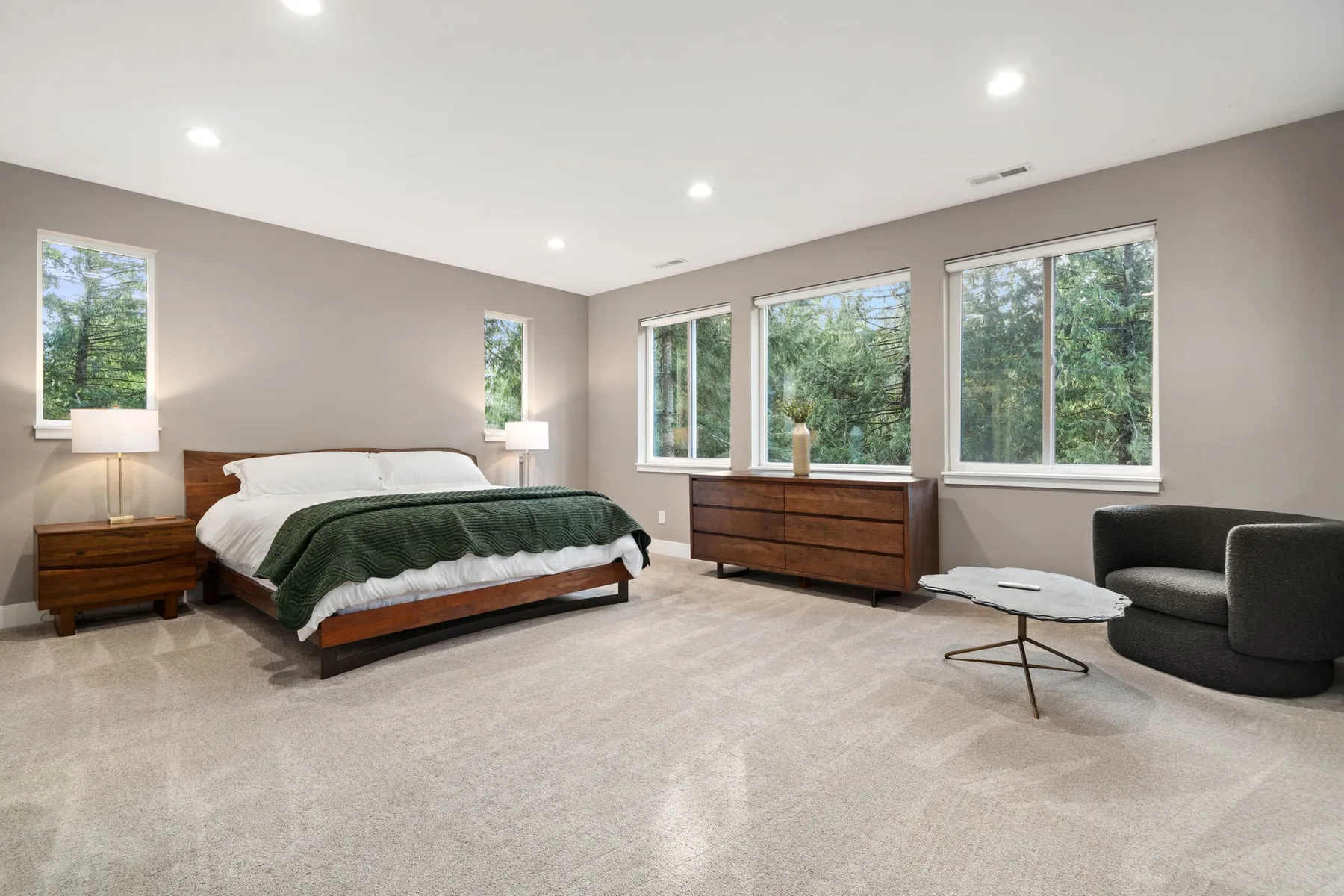 Un dormitorio con cama, cómoda de madera y grandes ventanas con vistas a la vegetación.
