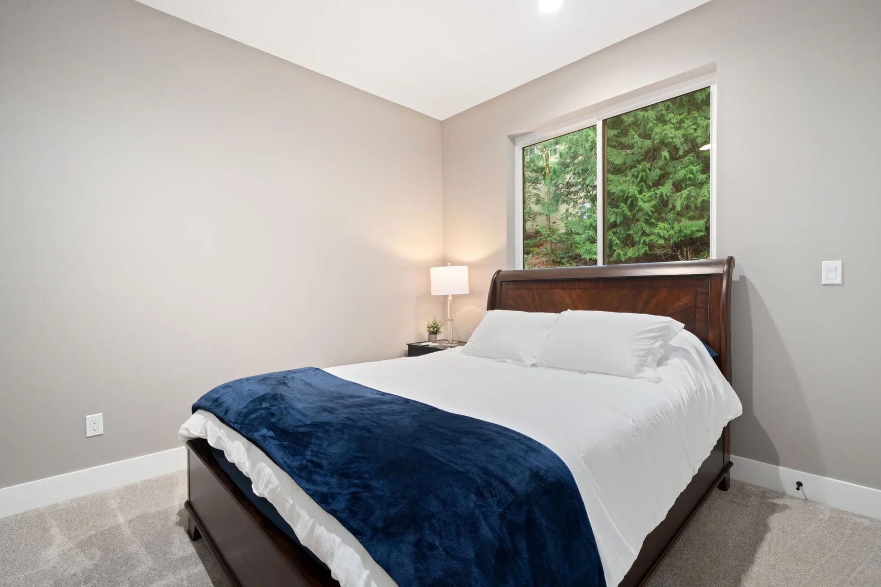 Un dormitorio luminoso con una cama bien tendida y una ventana con vistas a la vegetación.