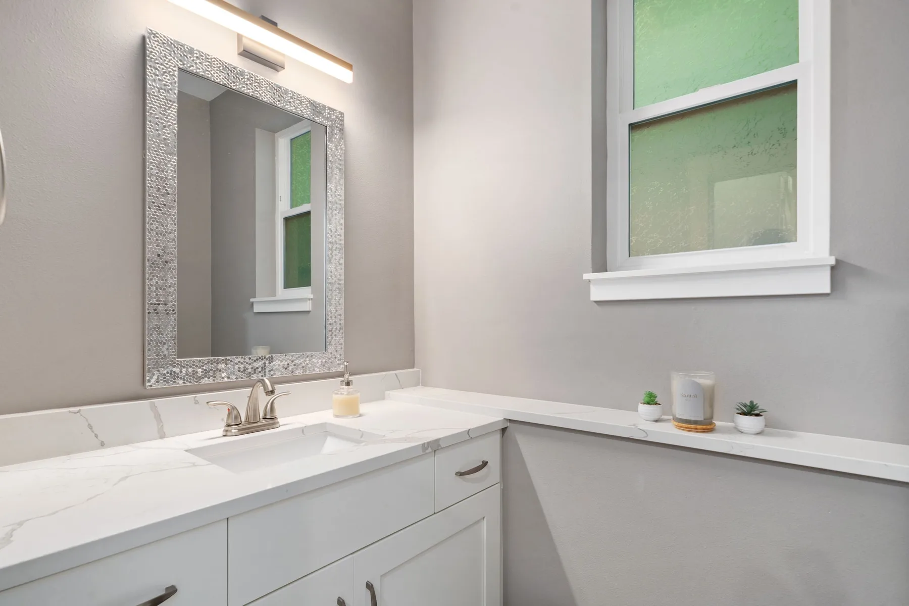 Un tocador de baño con un espejo grande y una ventana sobre la encimera.